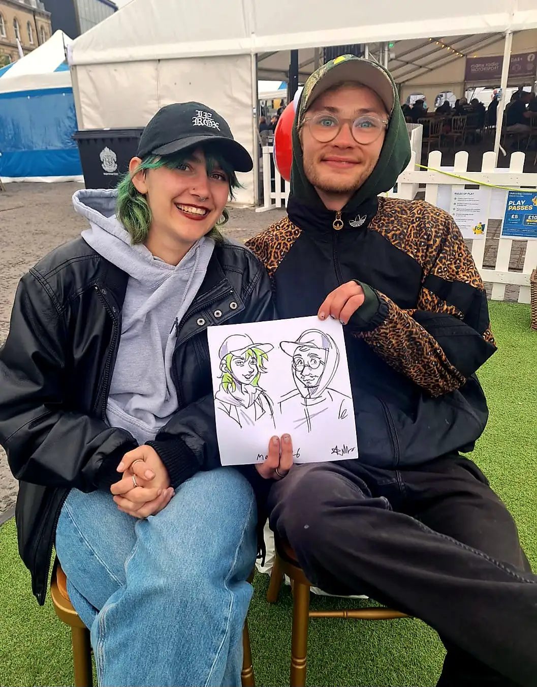 A couple showing off their finished cartoon portrait at an outdoor event