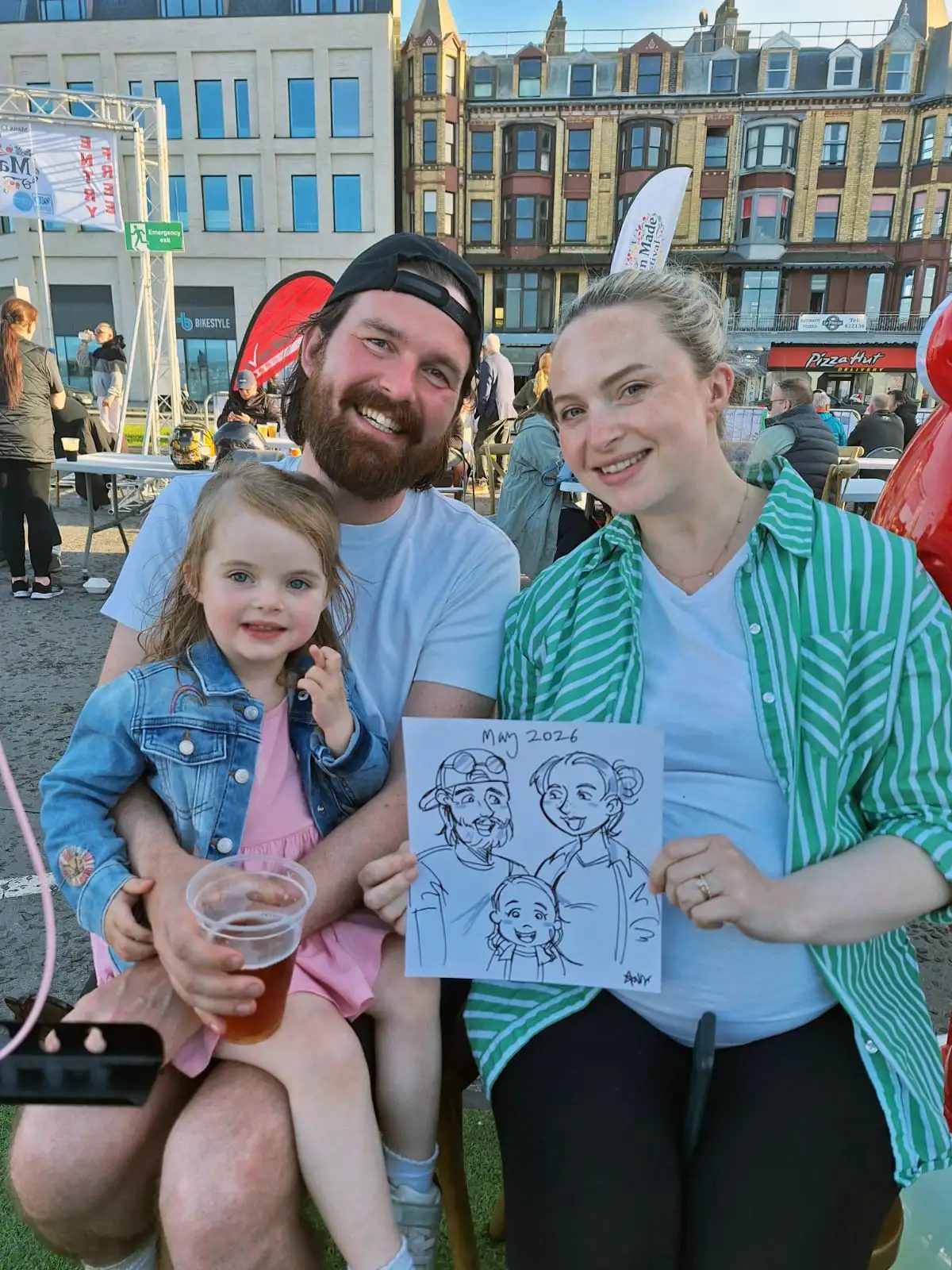 A young family holding up a cartoon portrait of the three of them