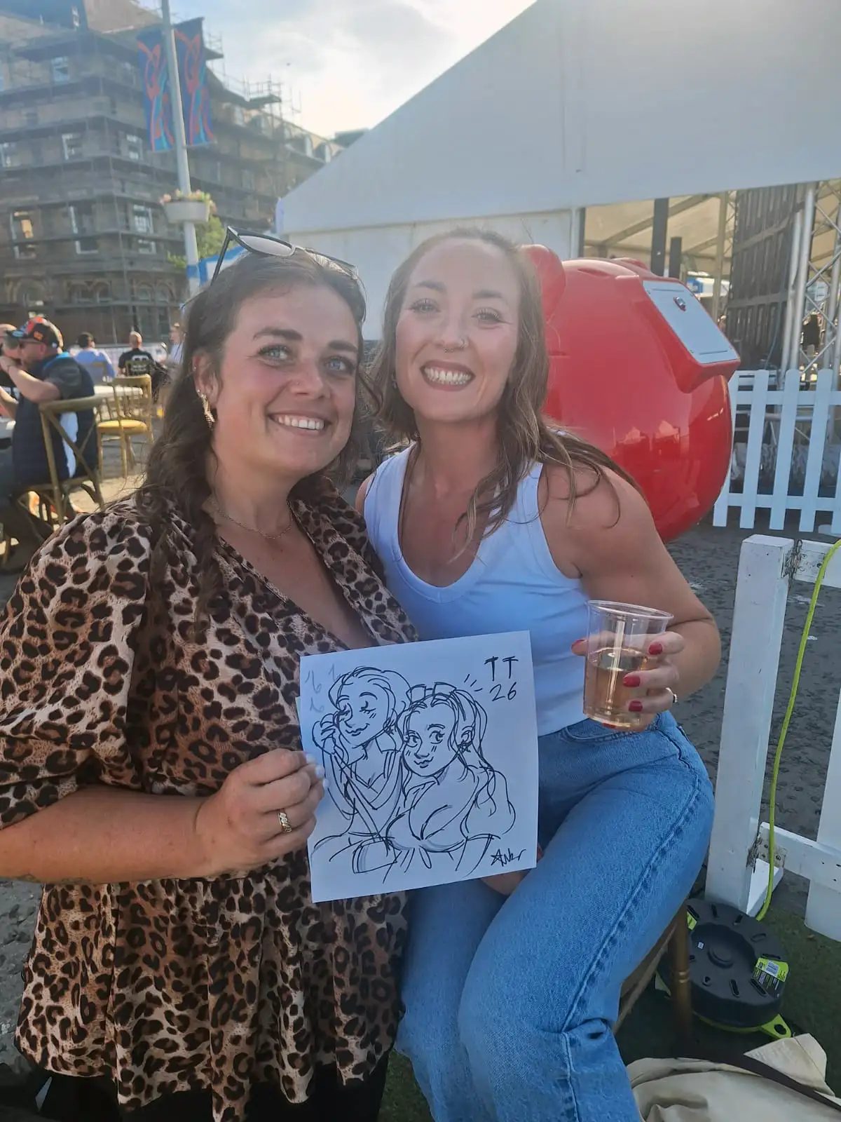 Two friends laughing with their cartoon portrait at an outdoor event