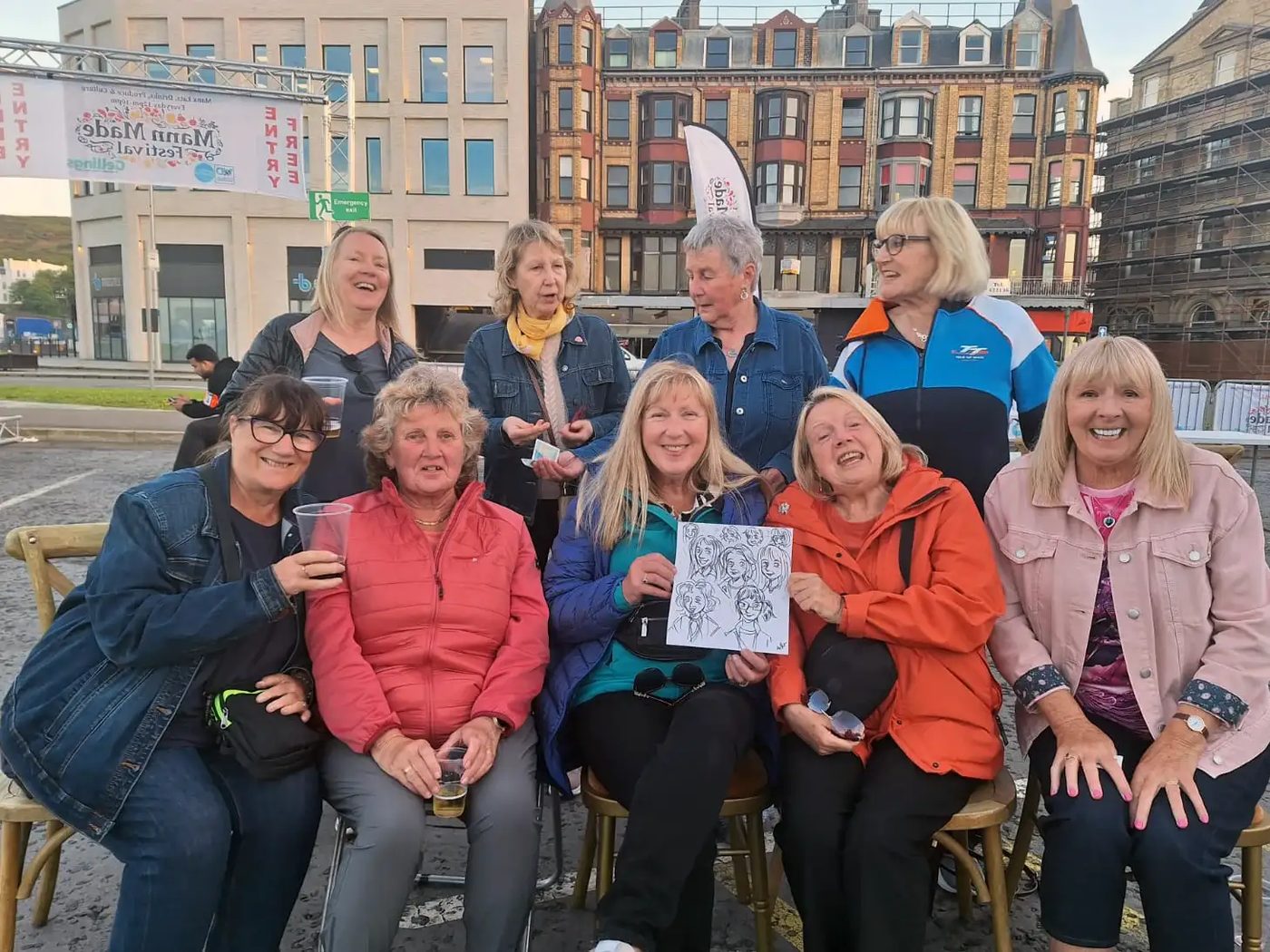 A group of friends laughing together with their finished group cartoon portrait at a festival