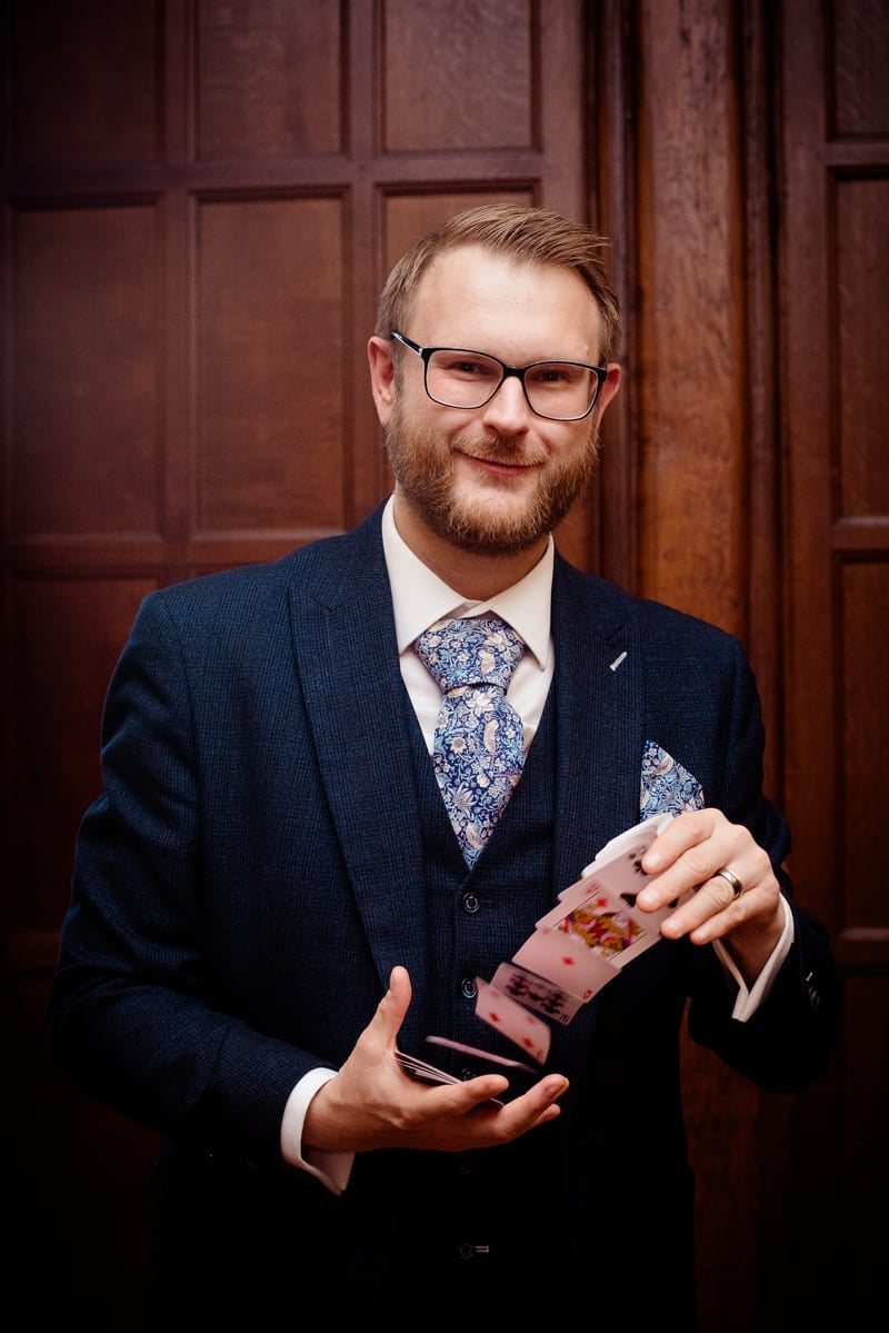 Chris, close-up magician, in a tailored three-piece suit holding a fan of playing cards