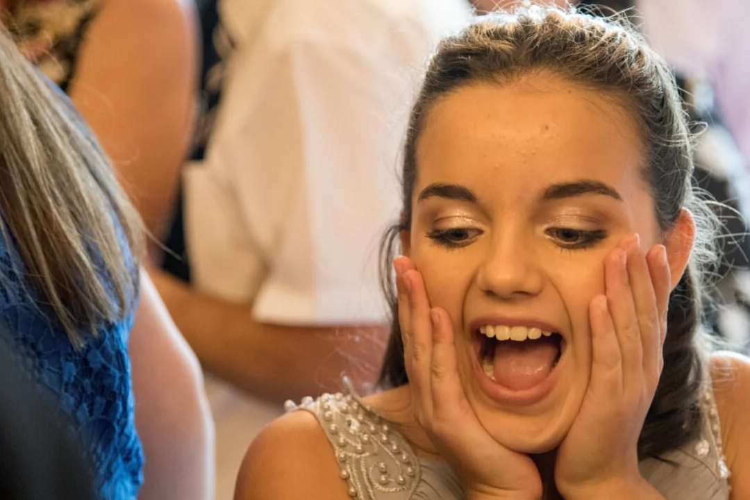 A young wedding guest with both hands on her face, stunned by a close-up trick