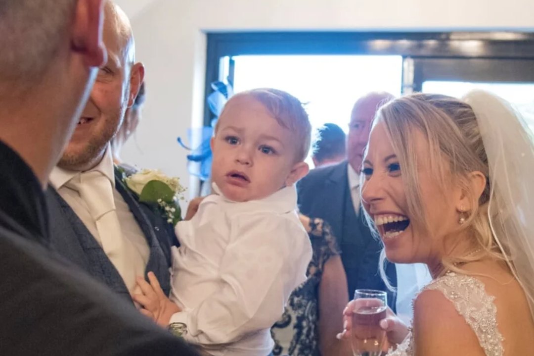 A bride holding a small child, laughing at a magic trick during the reception