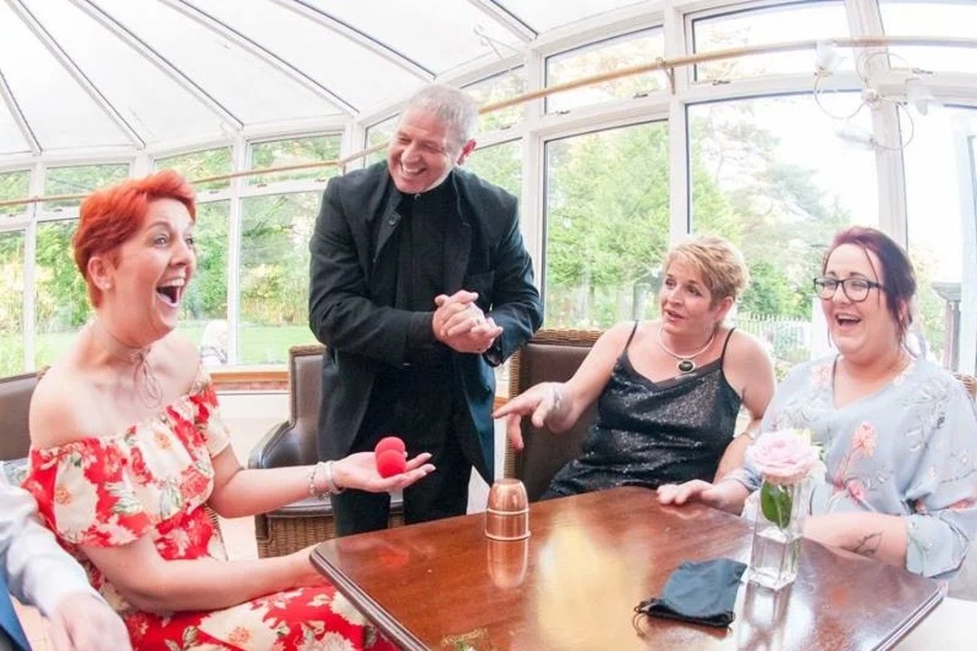Three seated guests laughing as the magician performs a close-up routine at a table