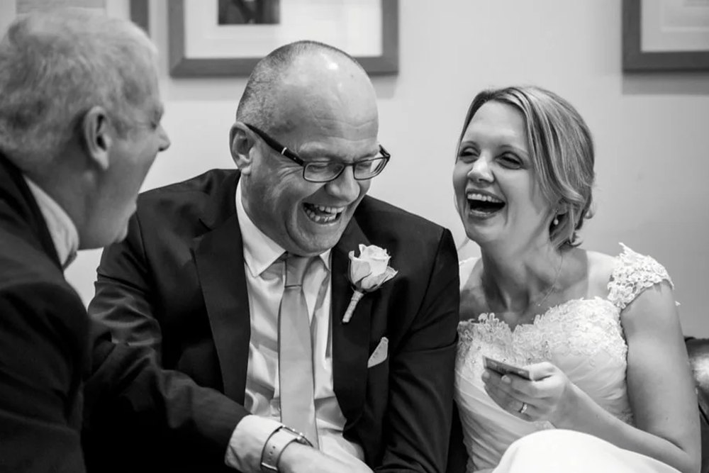 A black and white photograph of a bride and groom laughing during a card routine
