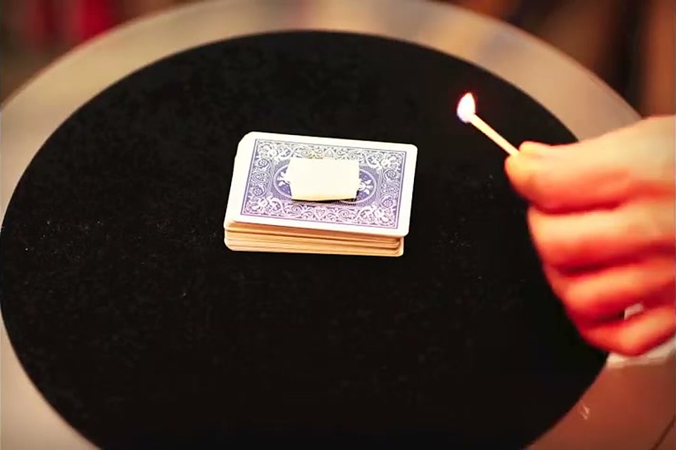 A lit match held over a pack of cards on a close-up mat