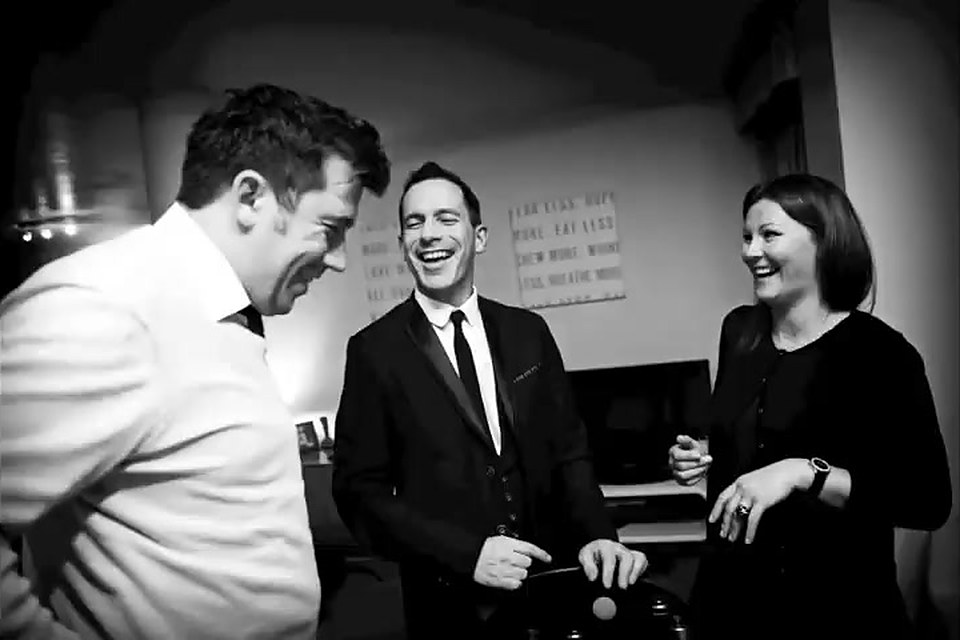 Two guests laughing as David performs close-up magic at a party