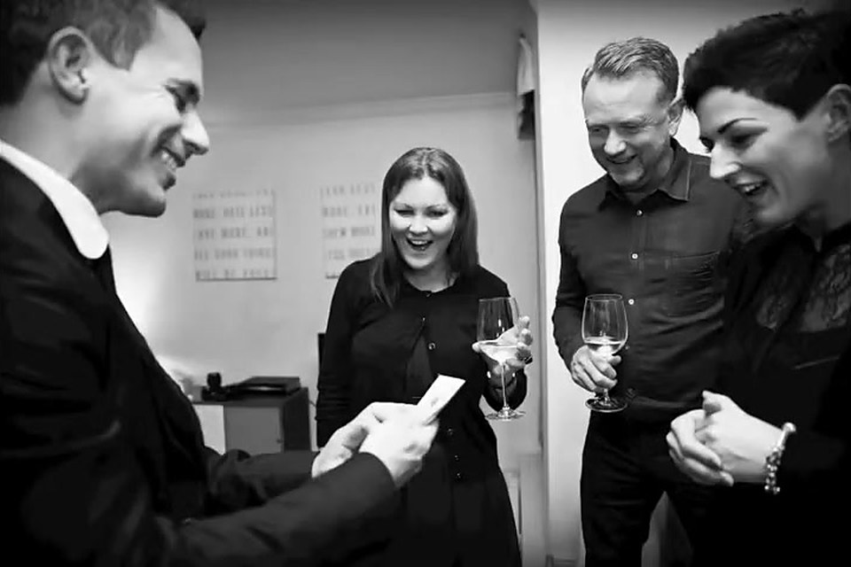 Standing guests laughing as the magician shows them a card
