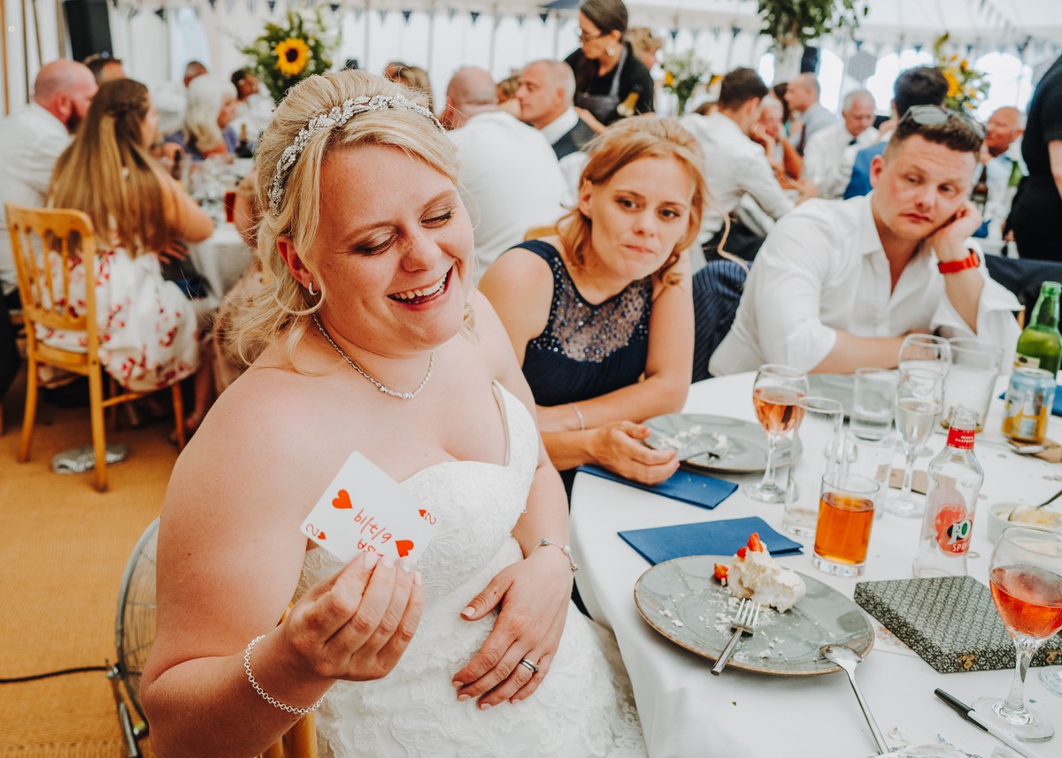 A bride laughing as she holds up her card at a wedding breakfast in Cornwall