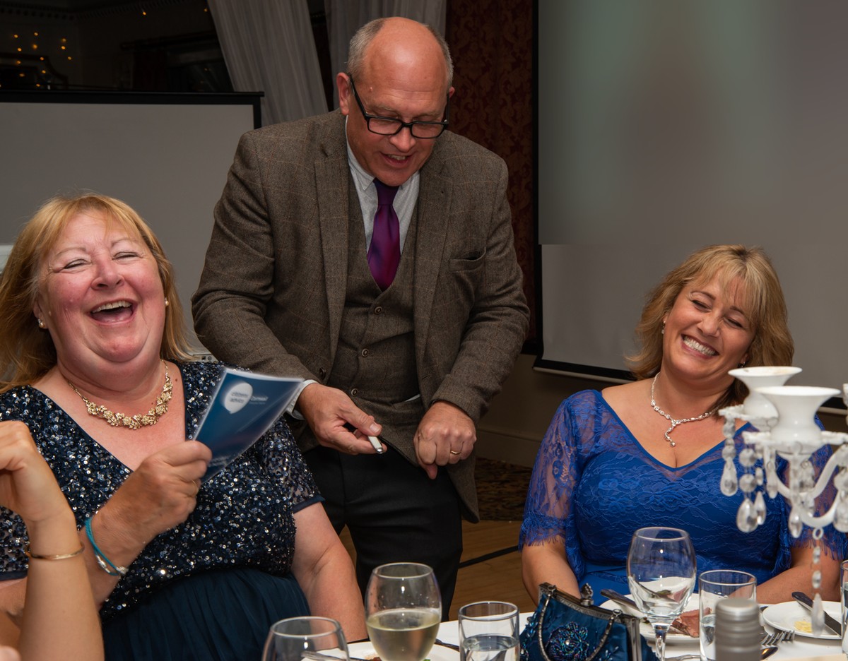 Two guests laughing out loud as Jack performs close-up magic at a dinner