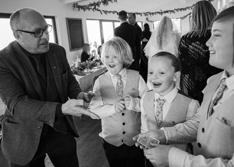 Two page boys laughing as the magician shows them a trick at a wedding