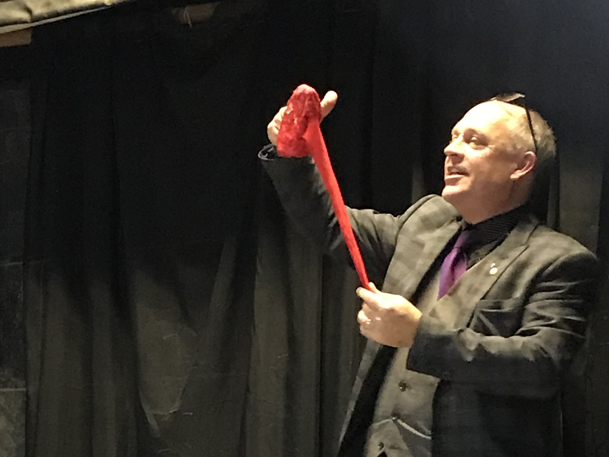 The magician on stage holding up a red rope during his stand-up show