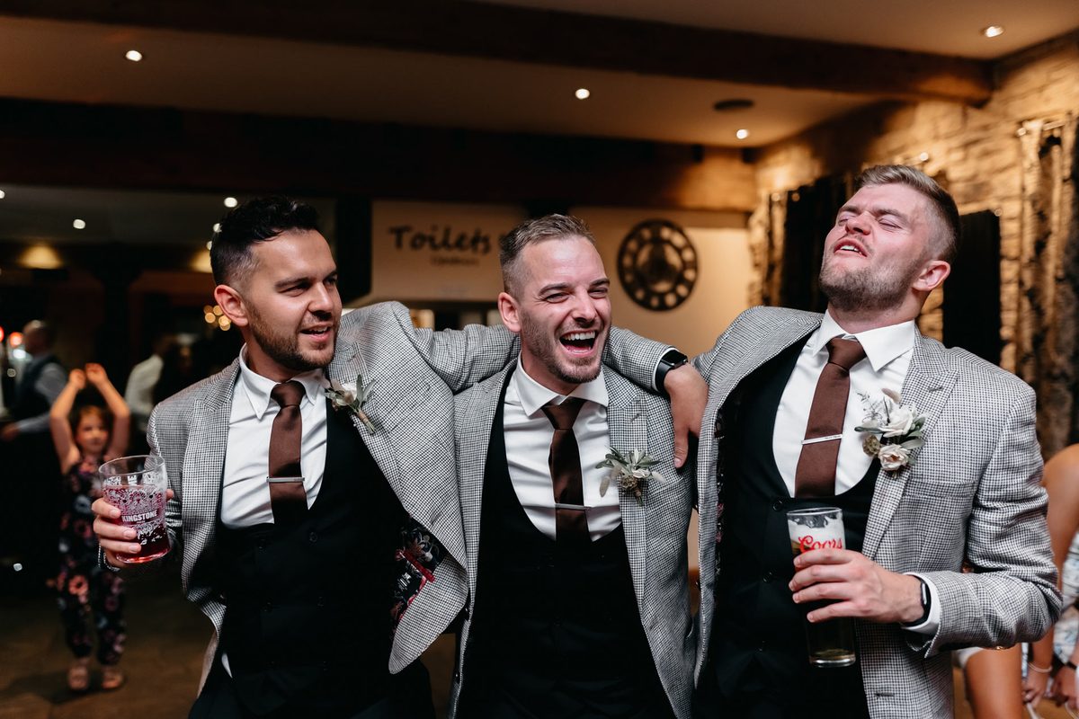 Groomsmen in grey suits laughing and cheering after a magic trick