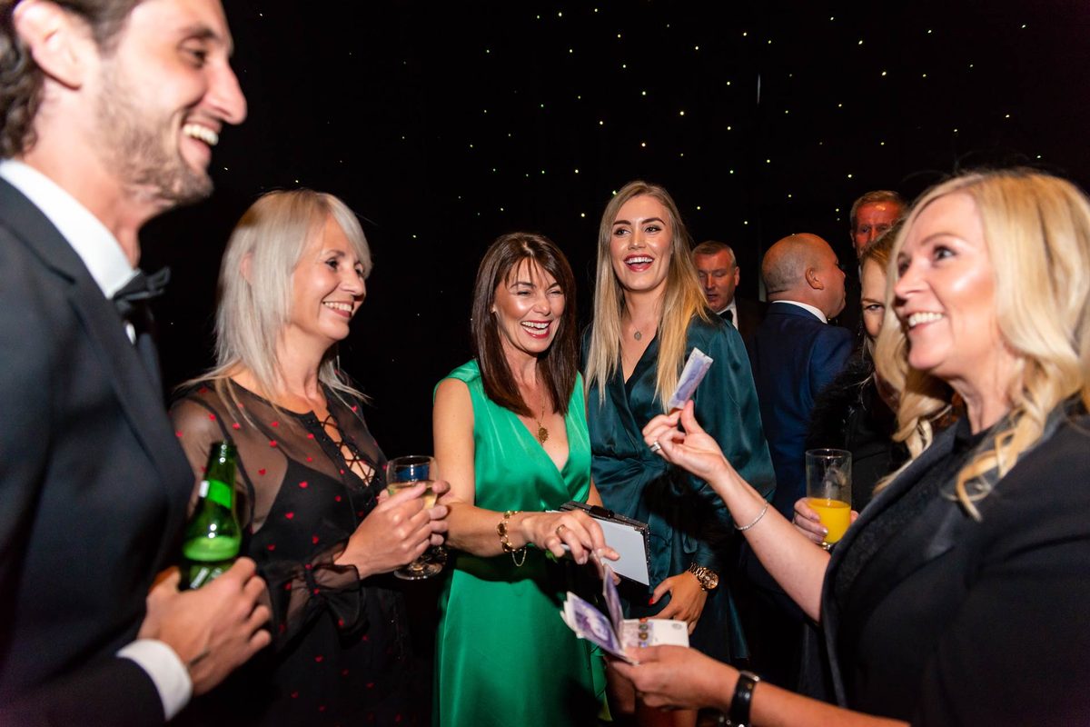 Guests at an evening party laughing as Aurora Myst performs a card trick