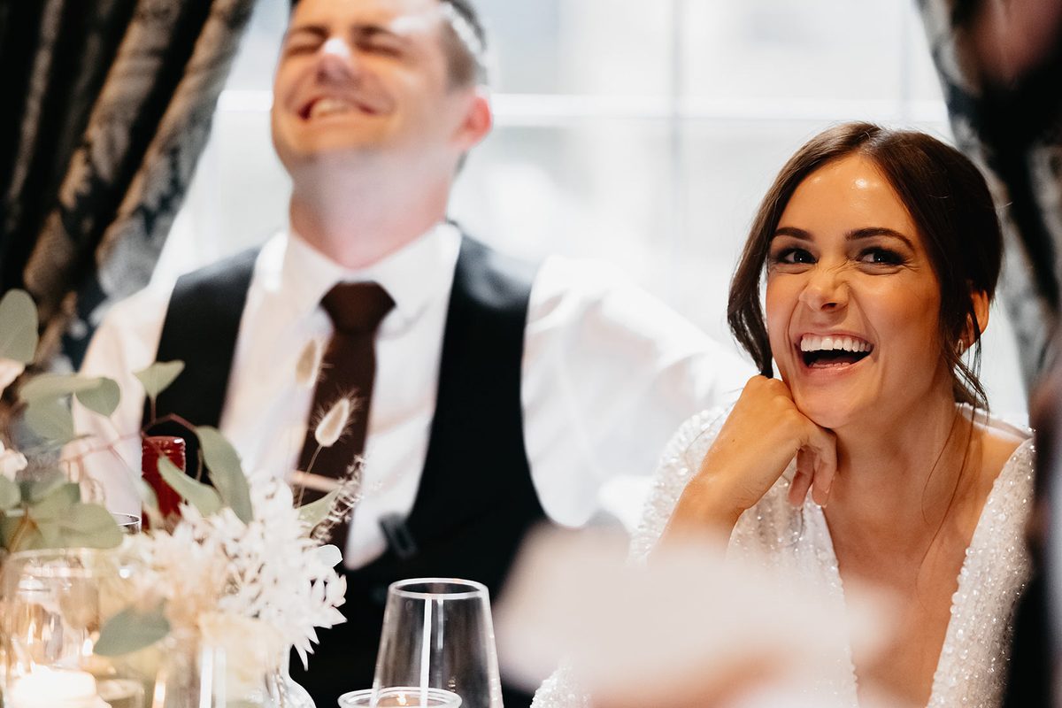 A bride and groom laughing at their wedding breakfast during a magic trick