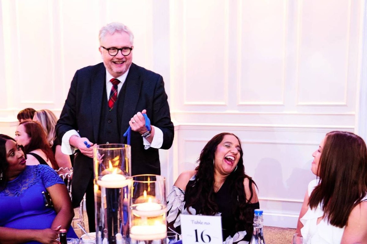 Banter Magic performing rope magic at a round table at a corporate awards dinner while a guest laughs
