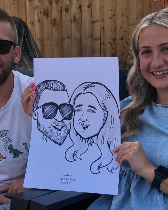 Couple holding their caricature at a garden party