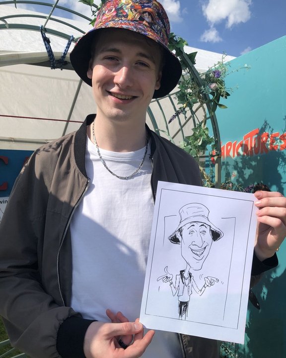 Guest in a bucket hat holding his caricature at a summer festival