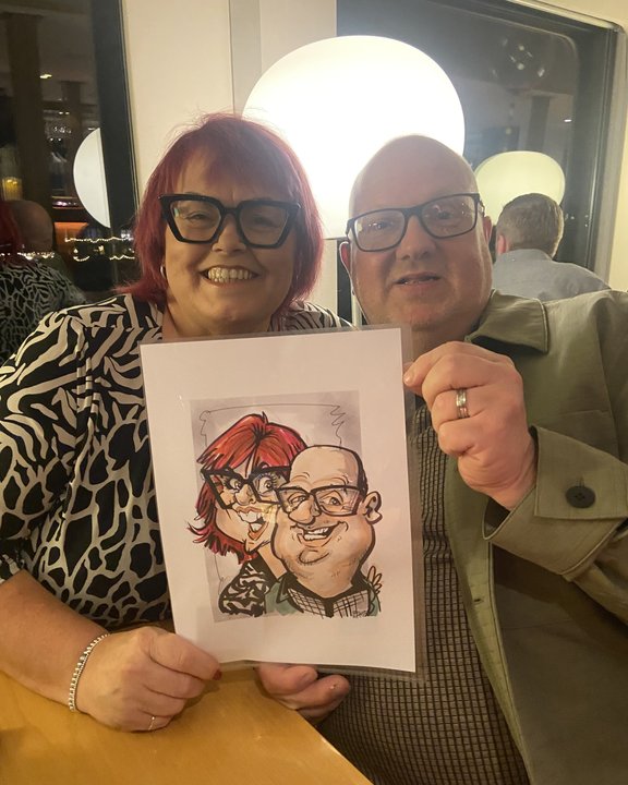 Couple in glasses holding their colour caricature at an evening party