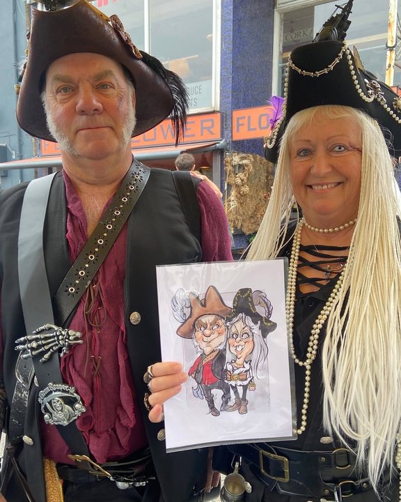 Couple in pirate costume holding their colour caricature at a summer festival