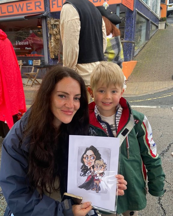 Mother and son holding their caricature at an outdoor festival