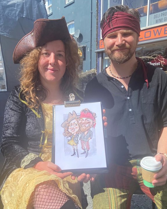 Couple in pirate costume with their colour caricature at a summer festival