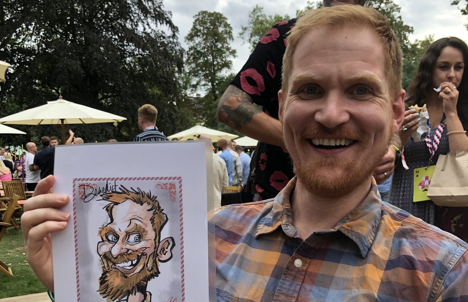 Smiling guest holding up his colour caricature at a summer garden party