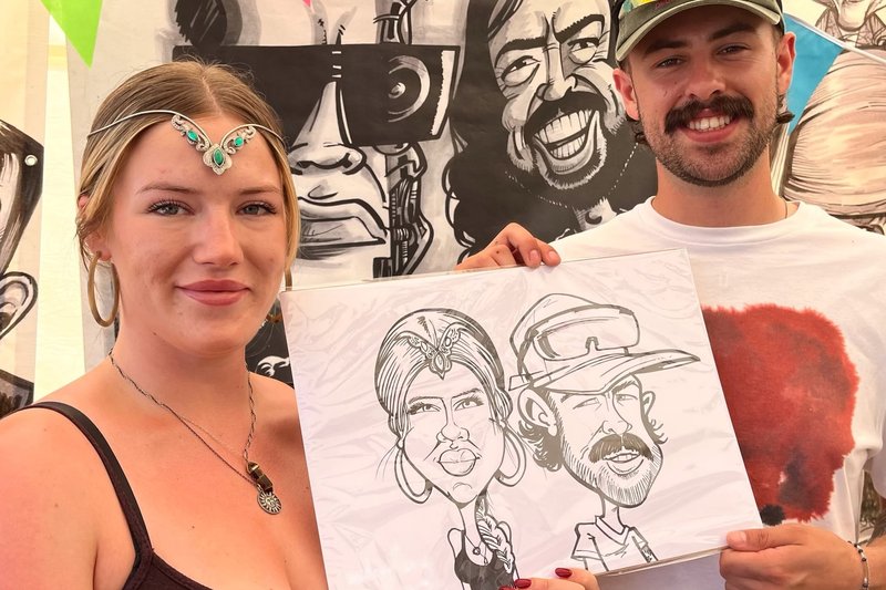Couple holding their caricature at a festival stall