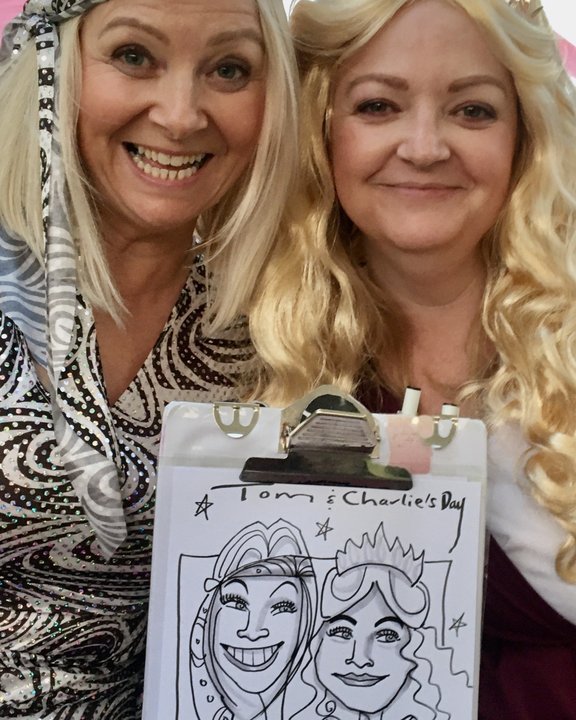 Two friends holding their shared caricature at a party