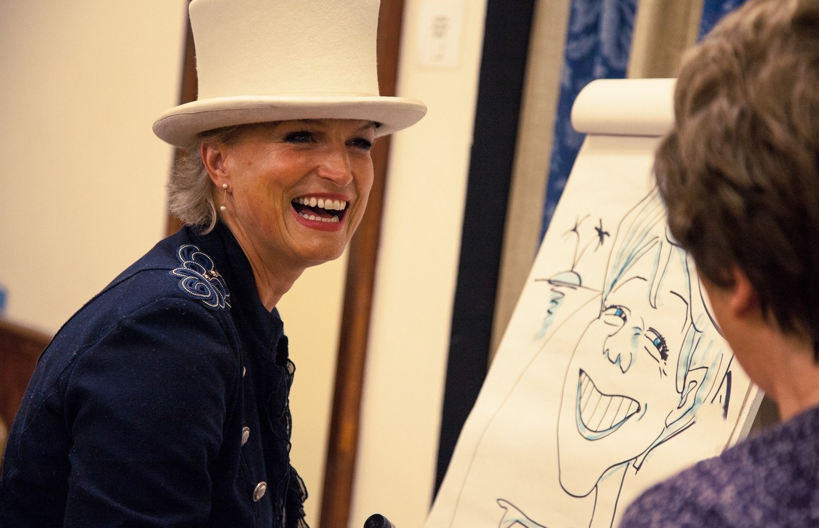 Dapper Caricatures artist in a white top hat laughing while drawing a live caricature