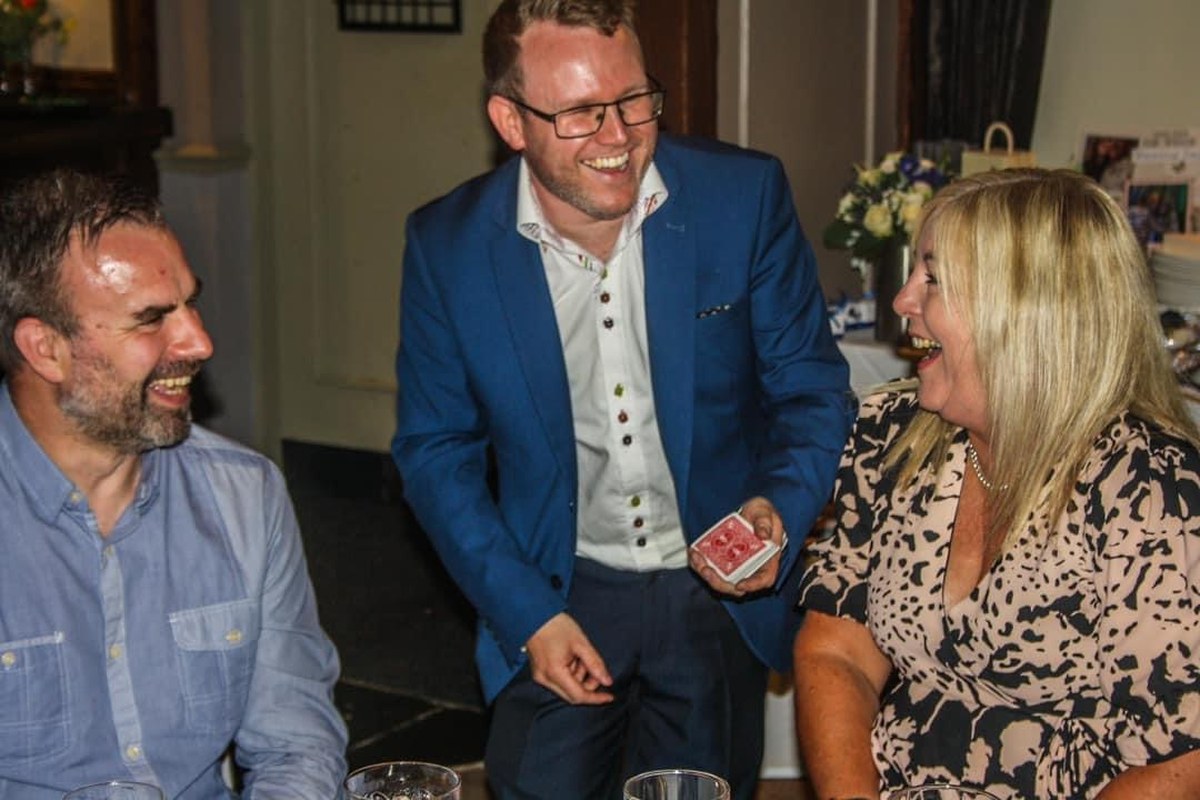 Double Take Magic, a close-up magician from Coventry, laughing with two guests at a table during a card trick