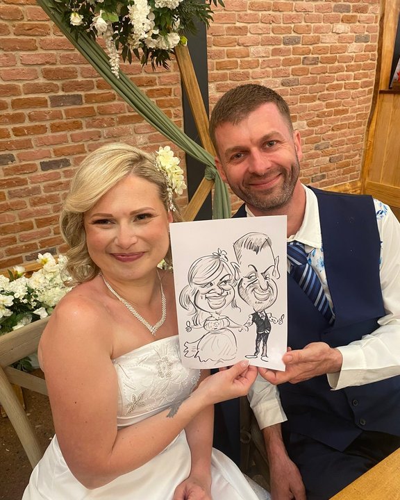 Bride and groom laughing with their caricature at the reception