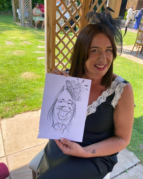 Wedding guest in a fascinator holding her caricature in the garden