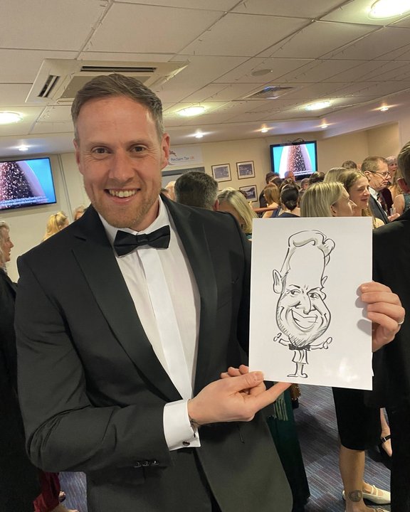 Guest in black tie holding his caricature at a charity gala