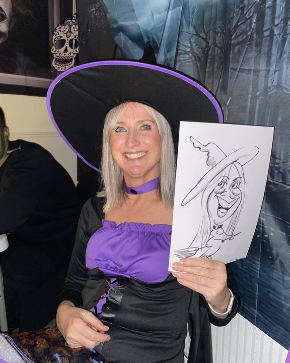 Guest in a witch hat holding her caricature at a Halloween party