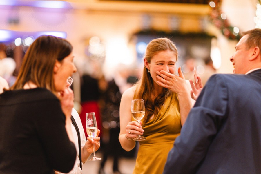 A guest in a gold dress covering her mouth in disbelief at an evening party