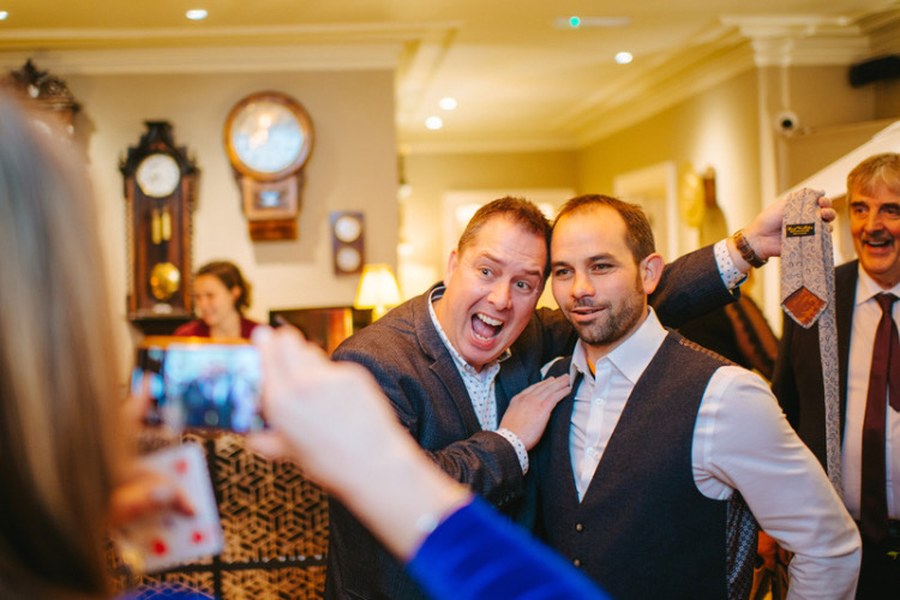 The Gentleman Pickpocket holding up a guest’s tie as the guest poses for a photo, unaware
