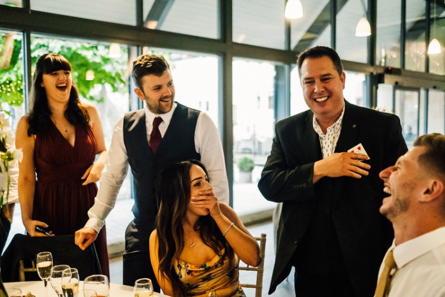 Wedding guests laughing at a table during close-up magic by the Gentleman Pickpocket