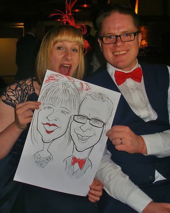 Wedding guest in a red bow tie and his partner holding their caricature