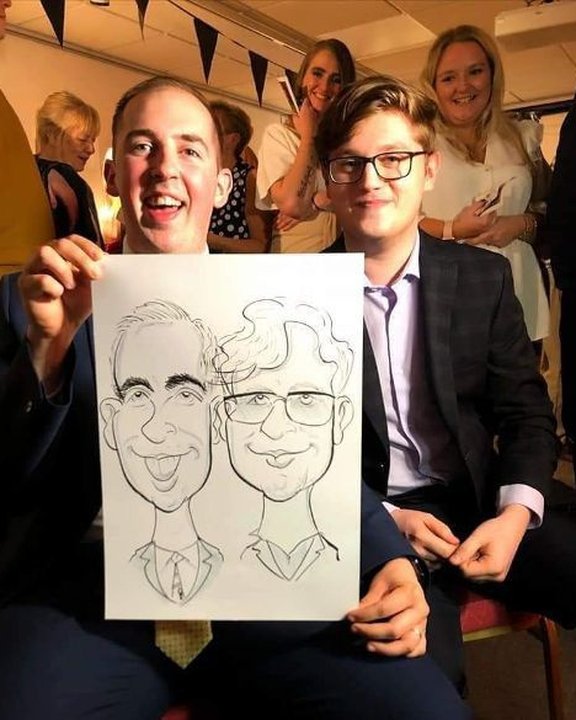 Two guests in suits holding their caricature at a party