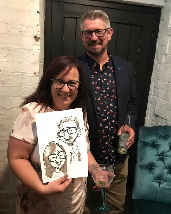 Couple holding their caricature at an evening party