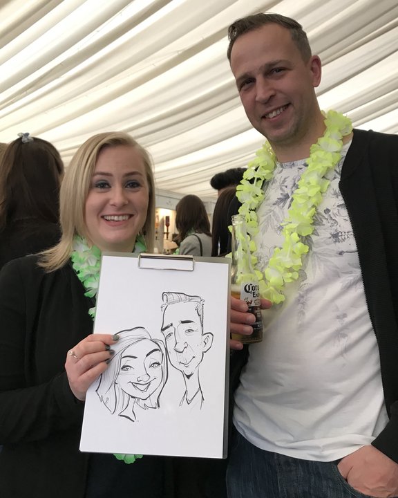 Couple in leis holding their caricature in a wedding marquee