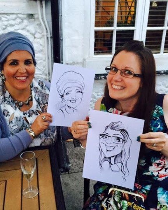 Two friends holding their caricatures in a pub garden
