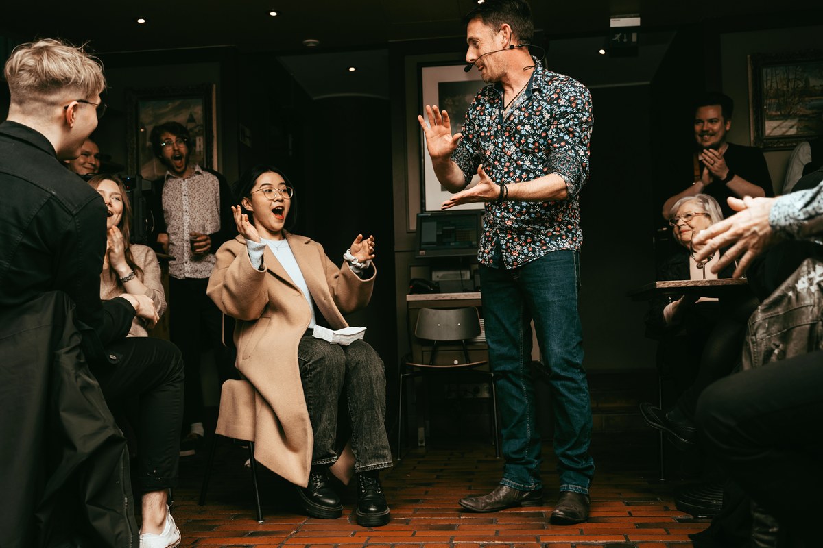 The Artful Pickpocket, a pickpocket and close-up magician, performing to a packed room as a guest leaps up in disbelief