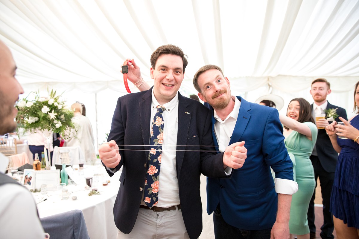 A wedding guest holding up the watch the Artful Pickpocket has just stolen from a groomsman without him noticing
