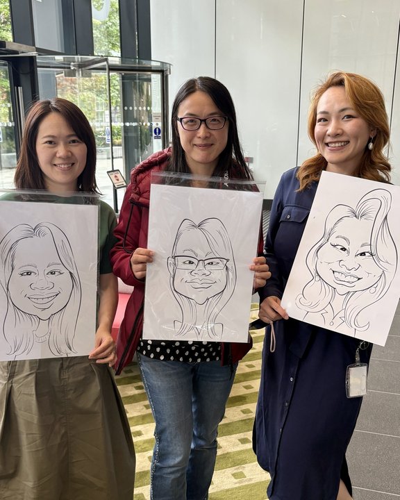 Three colleagues holding their caricatures at an office event