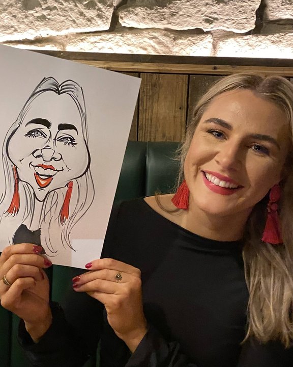 Guest in red earrings holding her caricature at a party