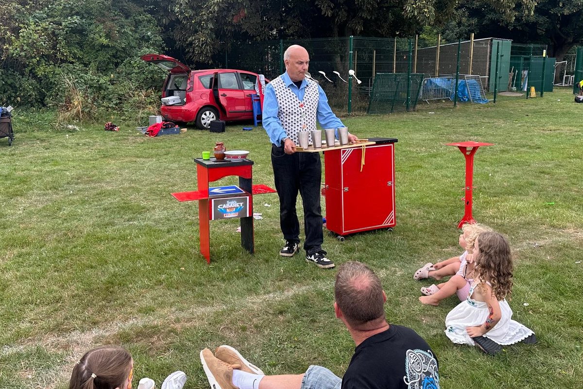 Families sitting on the grass watching Showtime Magic perform an outdoor magic show