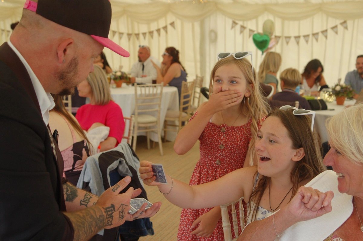 Young guests in a wedding marquee gasping at a card trick