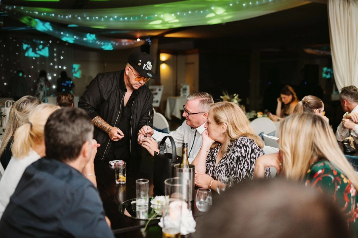 The magician performing table magic at a party under coloured lights